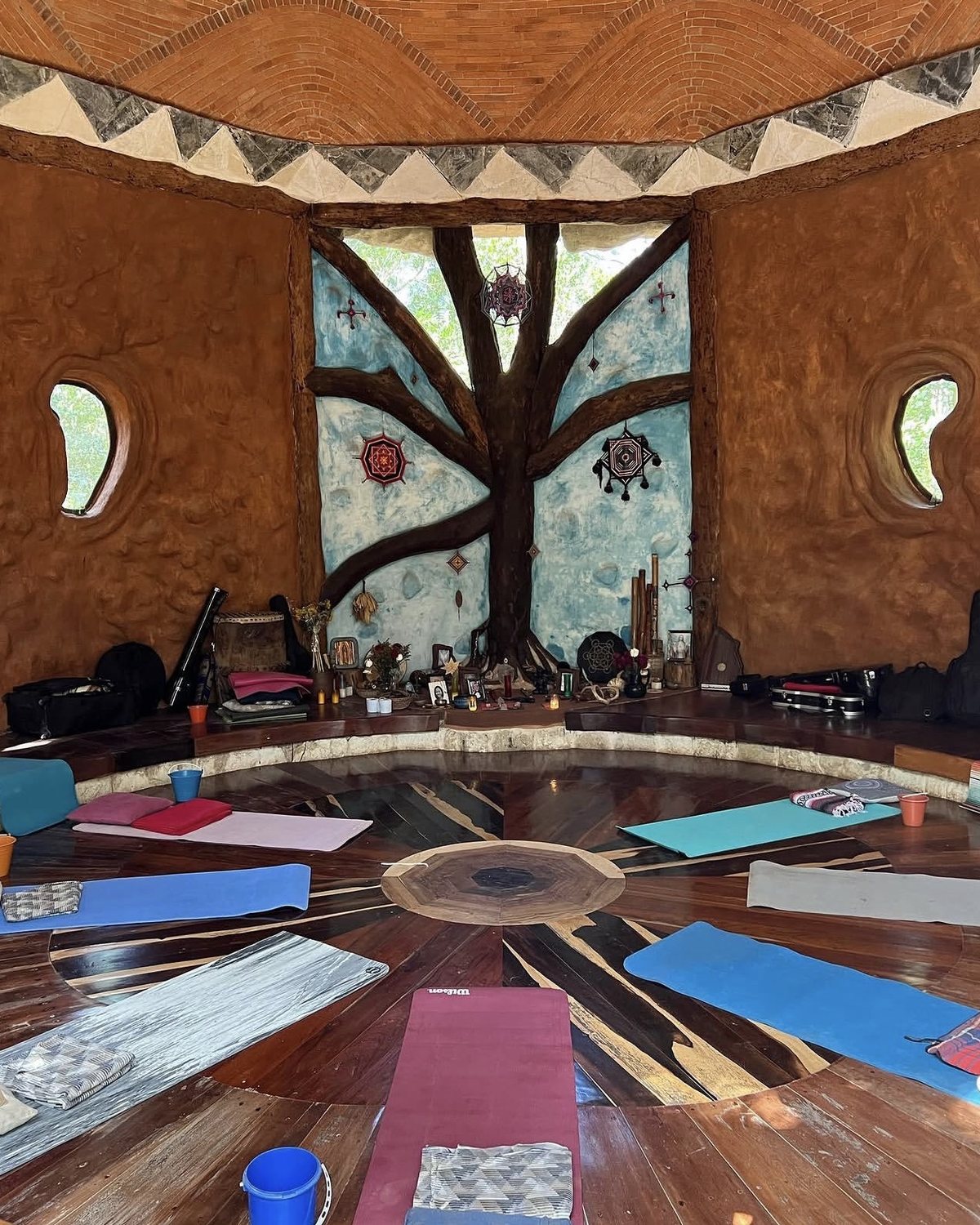 A round ceremony space with a carved tree mural and yoga mats arranged in a circle