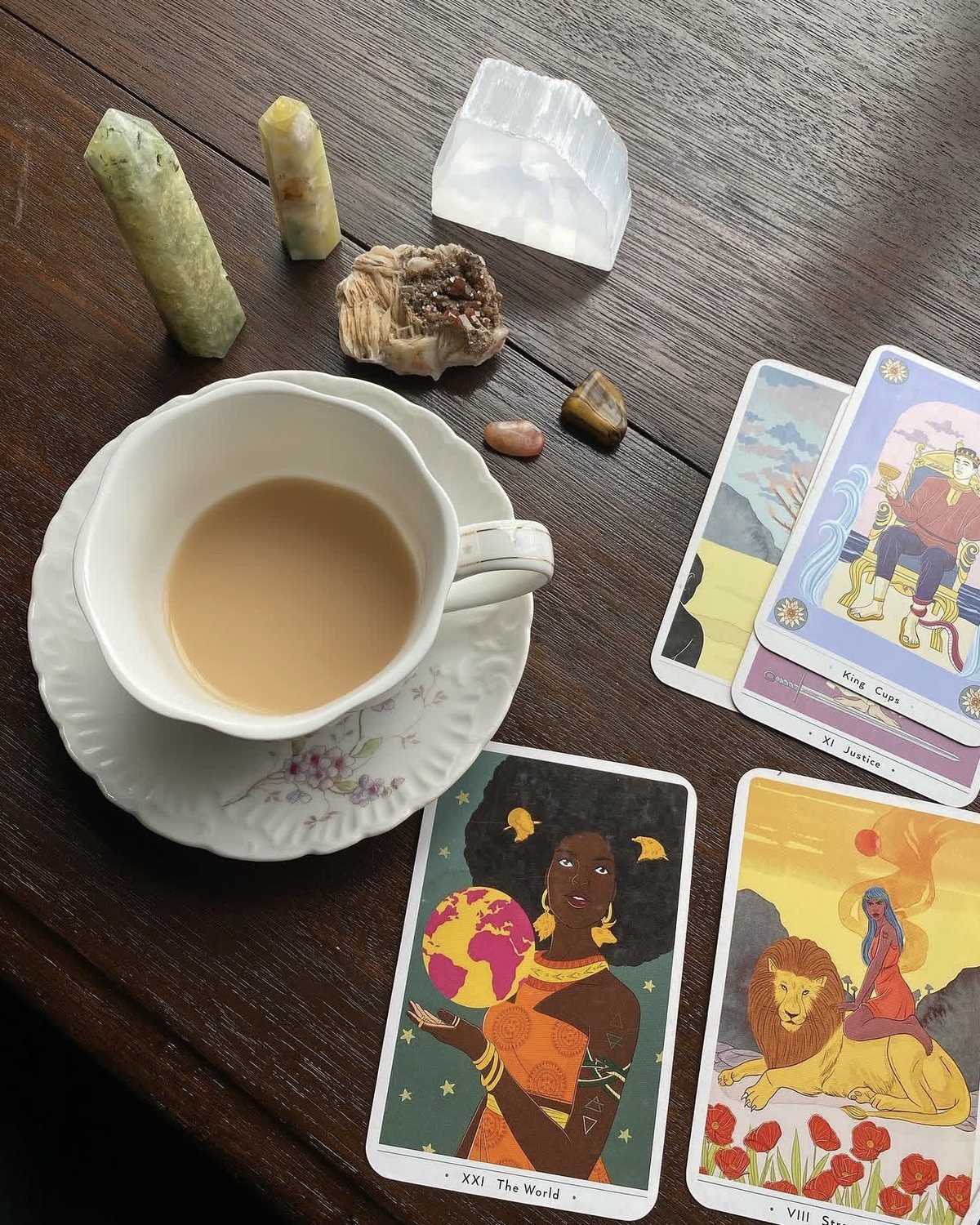 A cup of tea beside crystals and tarot cards on a dark wooden table